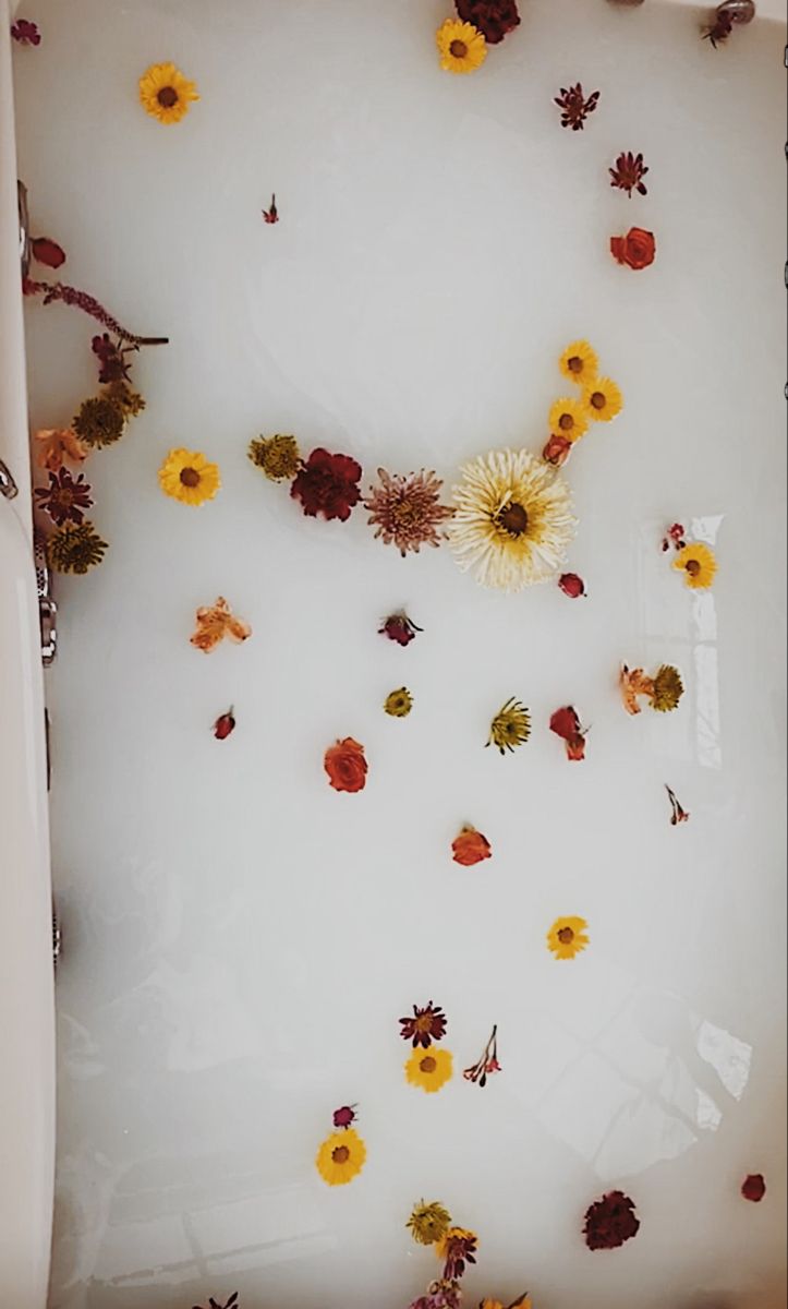 flowers floating in a bathtub with leaves and petals on the floor next to it