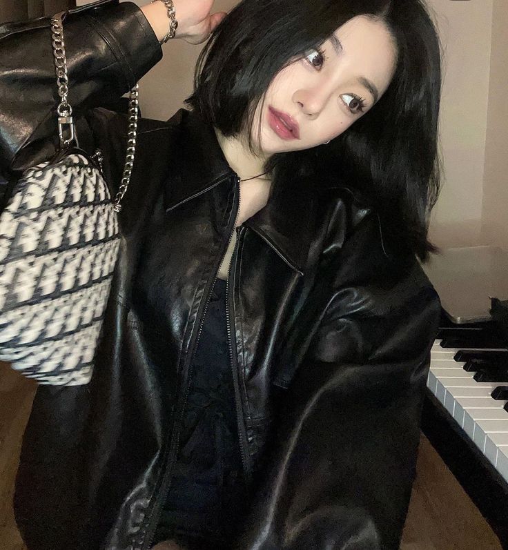 a woman with black hair wearing a leather jacket and holding a handbag over her shoulder