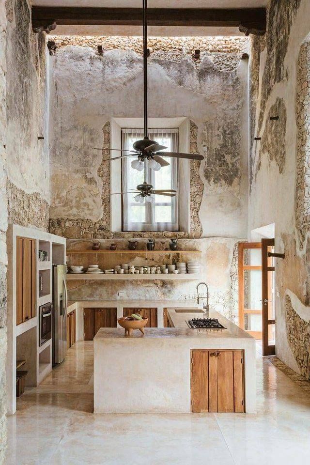 a kitchen with an island counter and ceiling fan in the middle, surrounded by stone walls