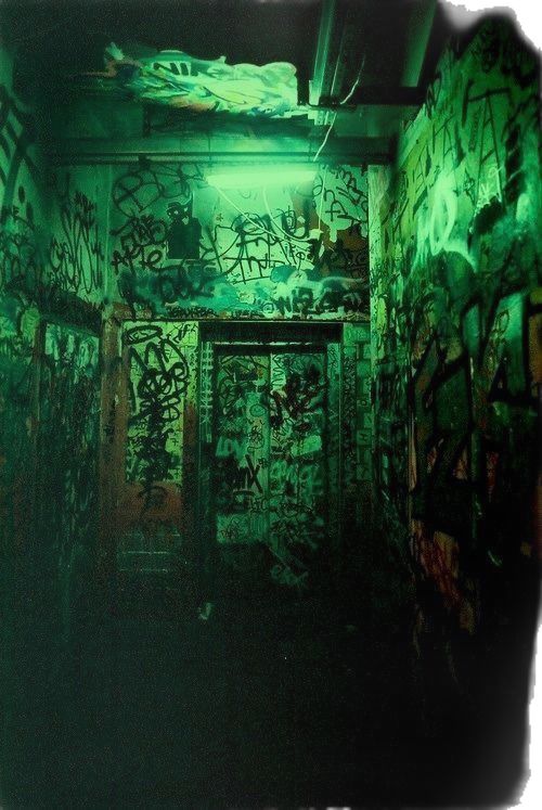 an old room with graffiti all over the walls and door to another room that is covered in green light