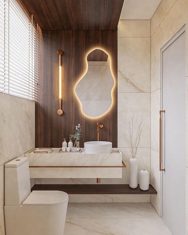 a white toilet sitting next to a bathroom sink under a light above it's mirror