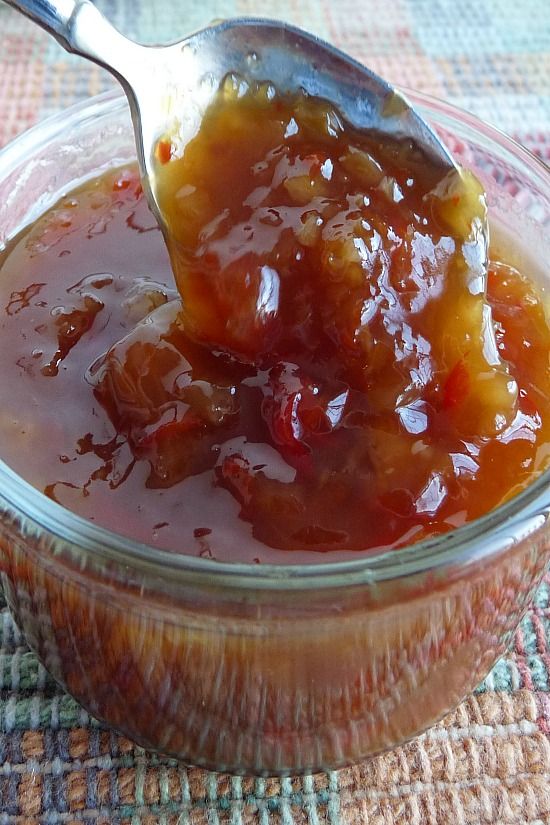 a spoon full of jelly sitting on top of a glass bowl filled with fruit jam