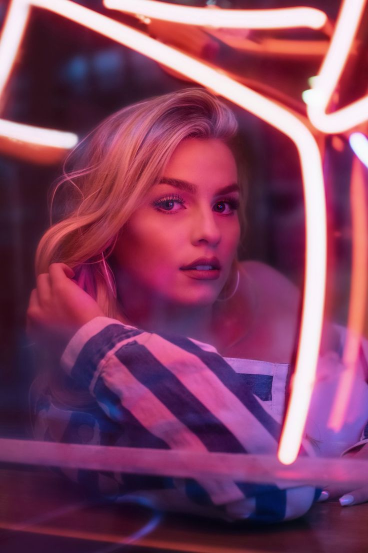 a woman sitting at a table in front of a neon light frame with her hand on her shoulder