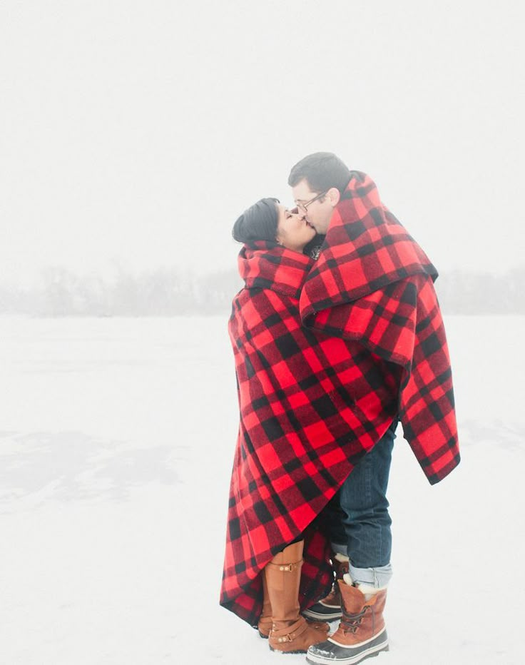 a man and woman wrapped up in a blanket on top of the snow covered ground