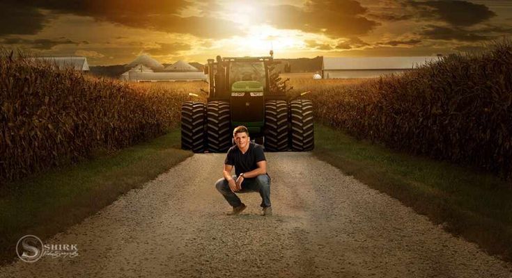 a man kneeling down in the middle of a dirt road next to a tractor and corn field