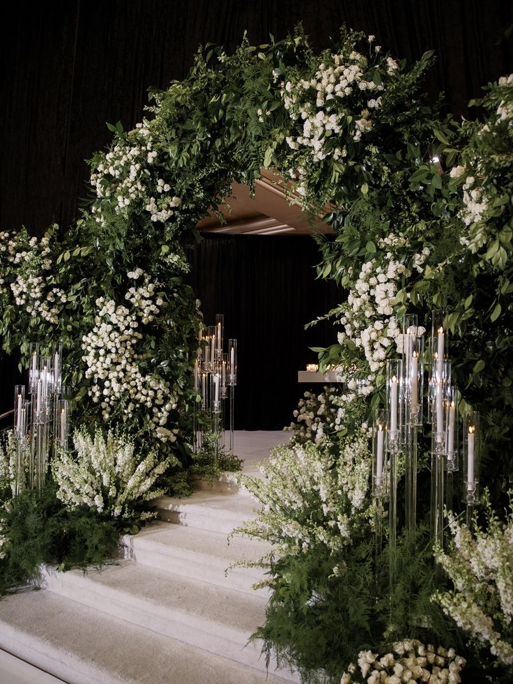 an archway with white flowers and greenery on the steps leading up to a stage