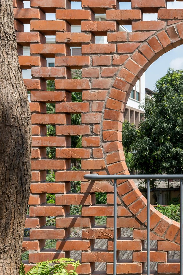 a brick wall with a circular hole in the middle and trees around it, as seen through a gate