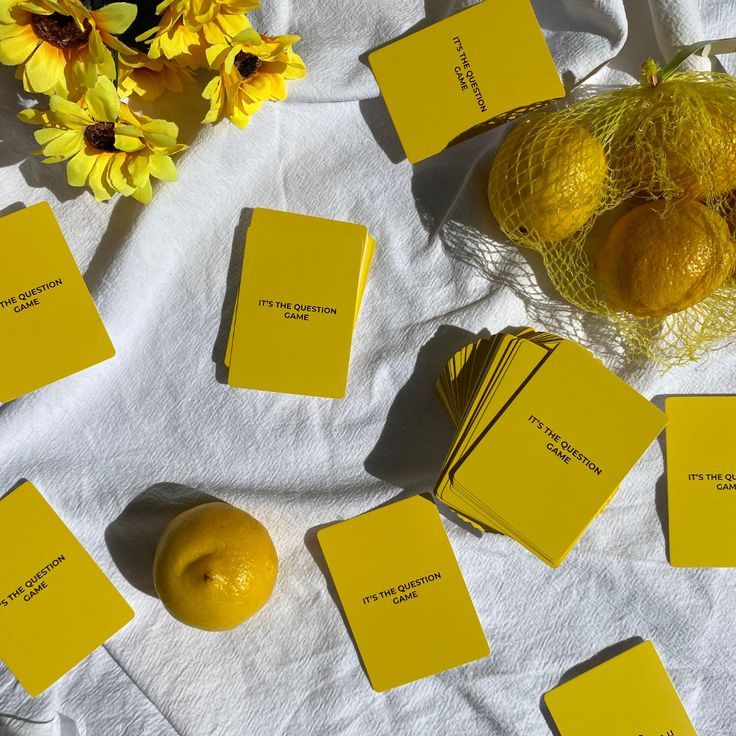 some yellow cards are sitting on a white tablecloth with flowers and lemons in the background