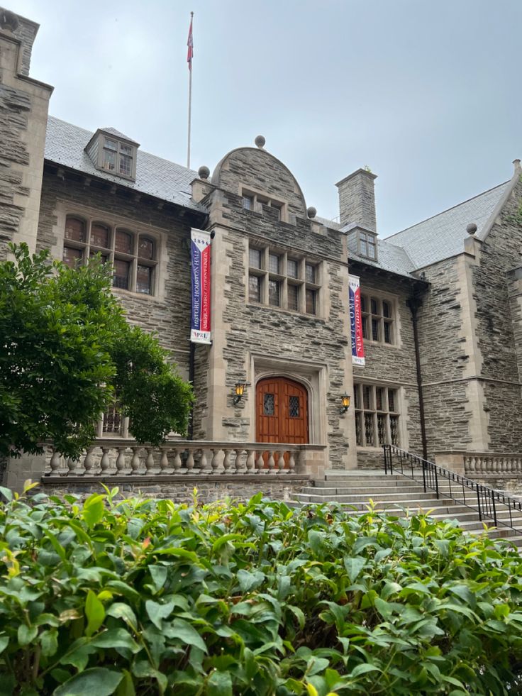 an old stone building with flags hanging from it's sides and bushes in front