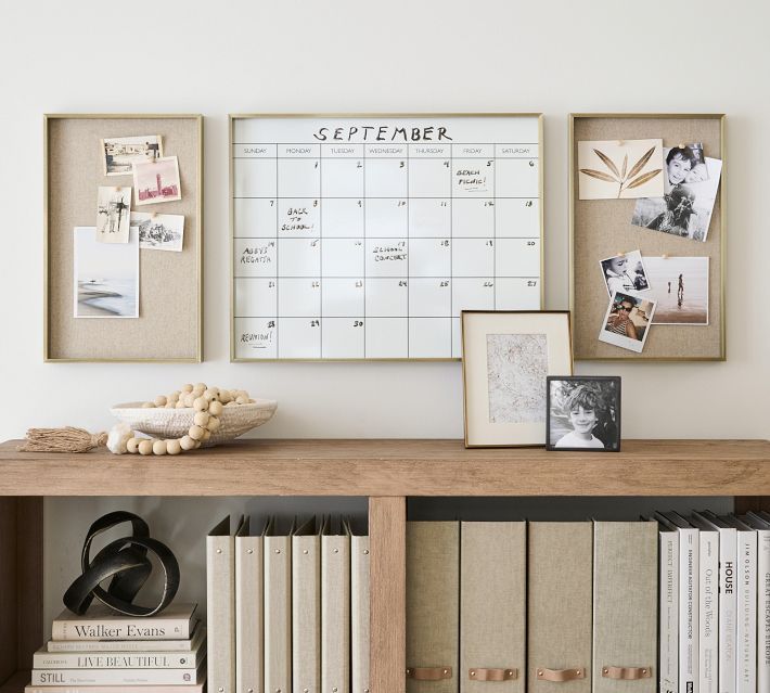 a wooden shelf topped with books and pictures next to a wall mounted calendar on the wall