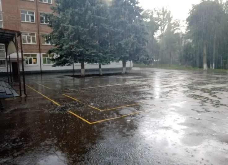 an empty tennis court in the middle of a rain soaked parking lot with trees on either side