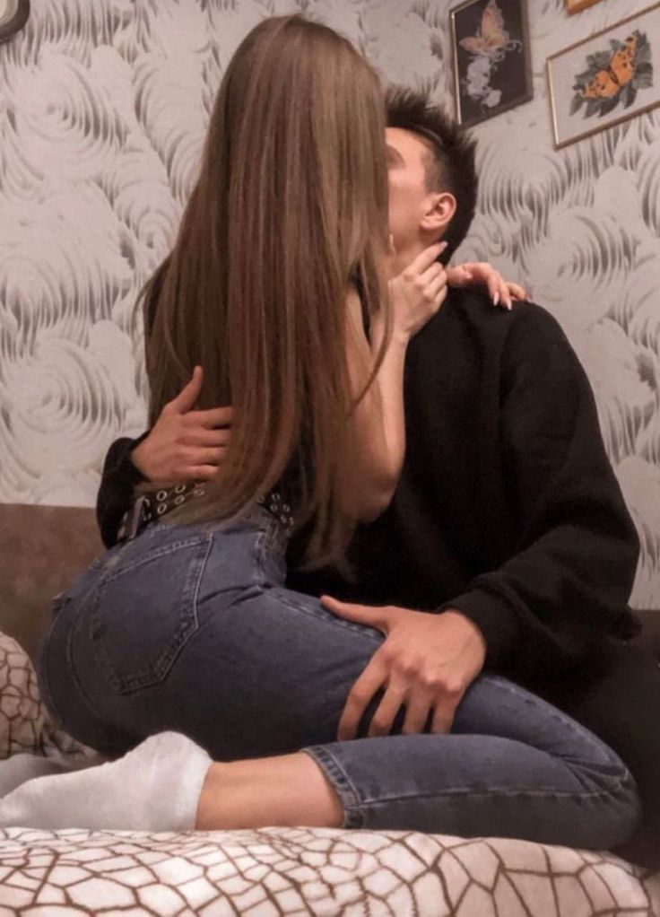 a man and woman sitting on top of a bed next to each other in front of a wall