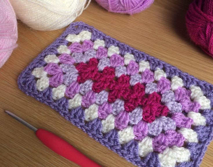 a crocheted square with hearts on it sitting next to yarn and knitting needles