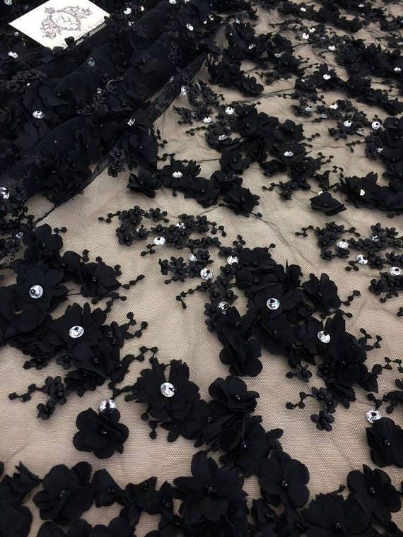 black flowers and sequins are scattered on a sheer - knit fabric, which has been draped over