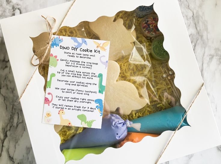 a cookie kit with dinosaur cookies in it on top of a marble countertop next to a note that says, do you try cake kits?