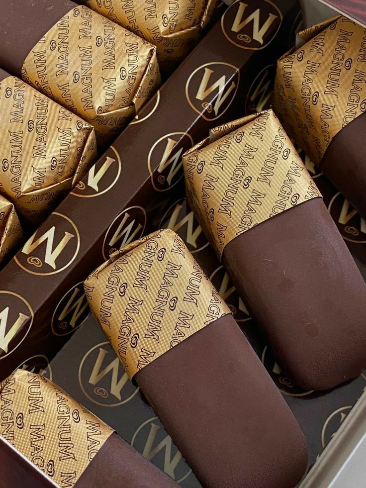 there are many pieces of chocolate in the box with gold foil on top and brown wrappers around them