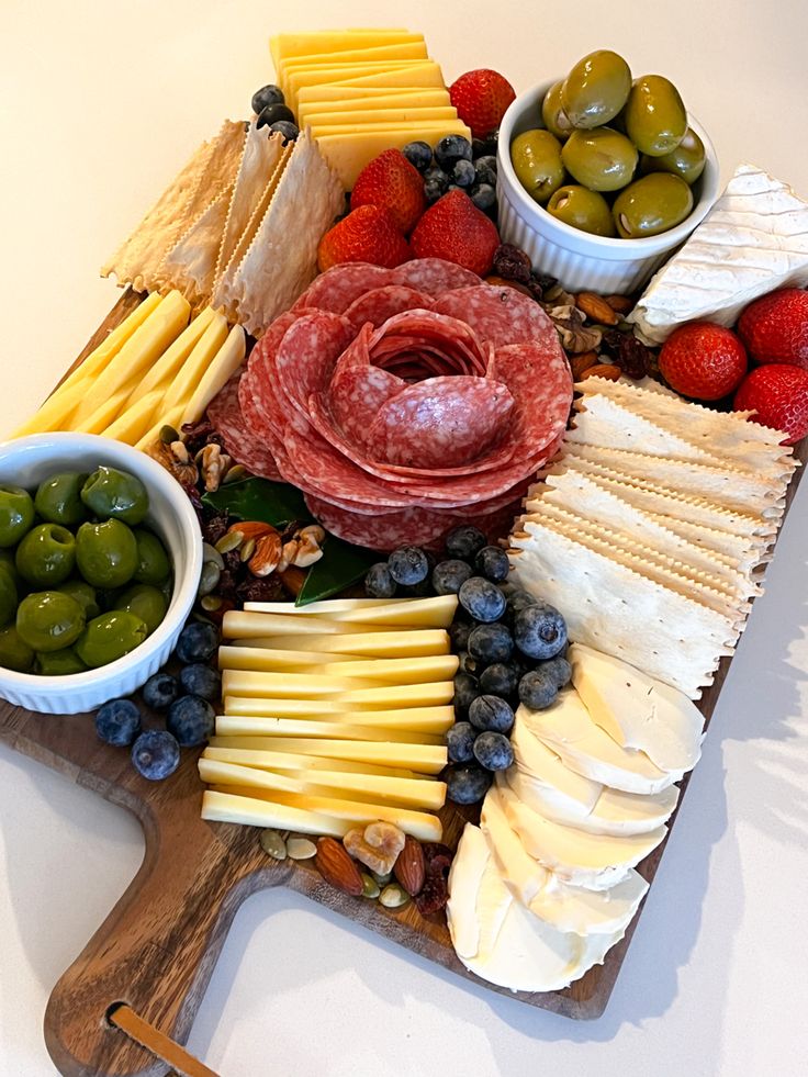 an assortment of cheeses, fruits and meats on a cutting board with olives