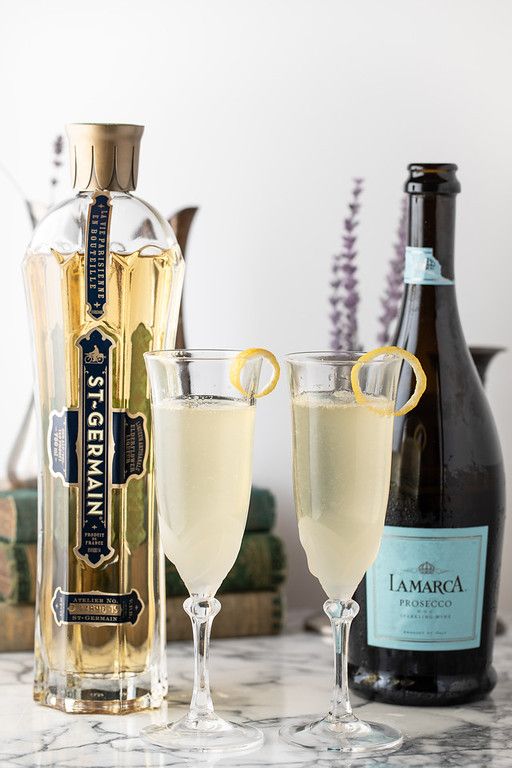 two champagne flutes are sitting on a marble counter top next to bottles of wine and a bottle opener