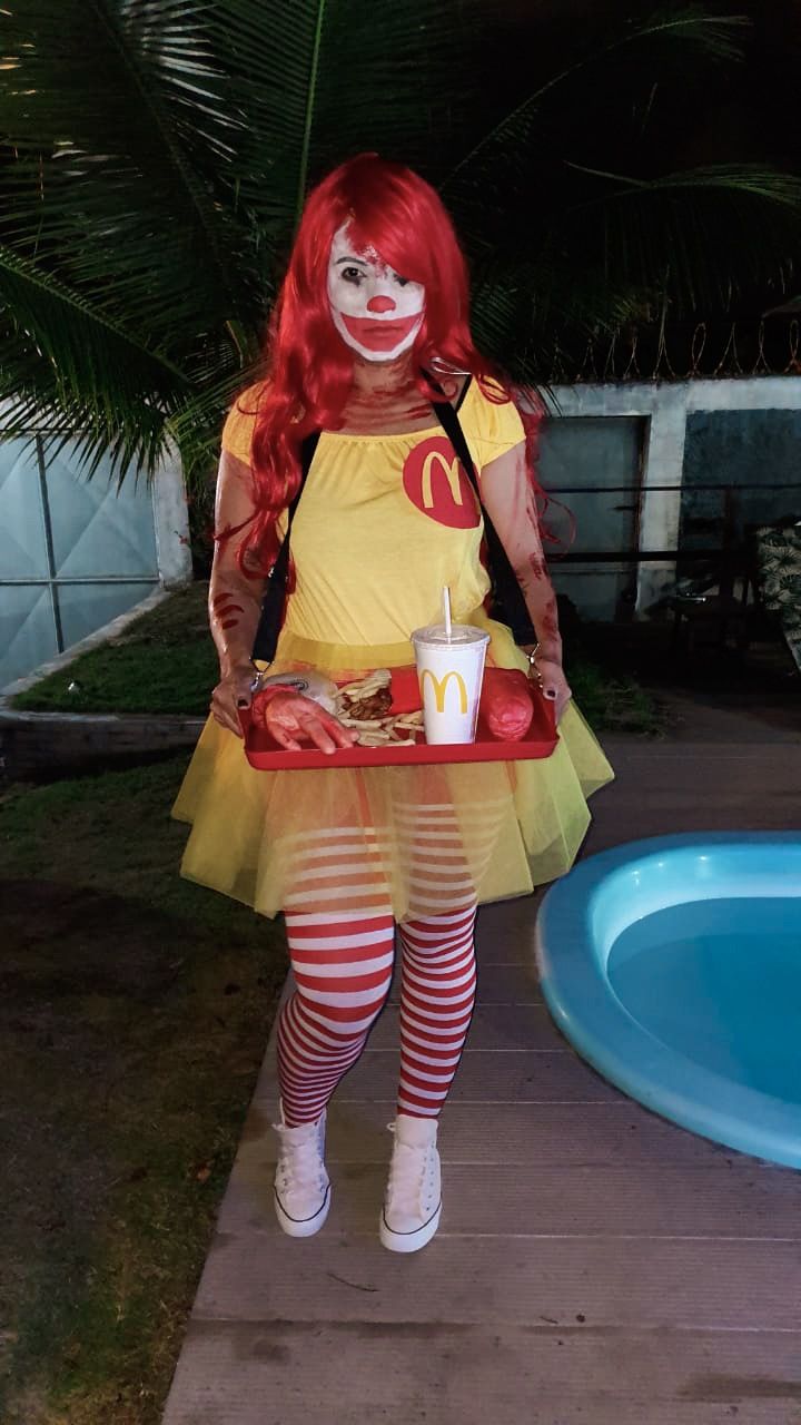 a woman dressed up as a clown holding a tray of food and a drink in her hand