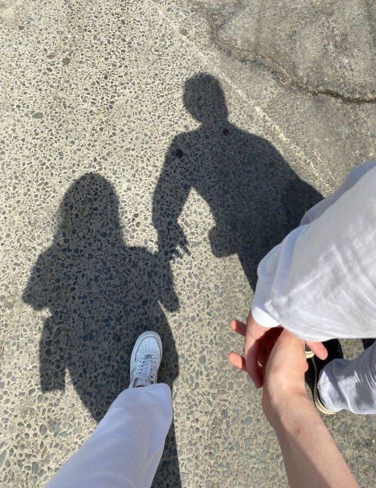 two people standing next to each other with their shadows on the ground and one person holding his hand