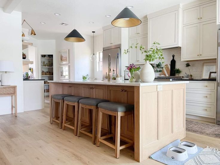 a kitchen with wooden floors and white cabinets, an island counter has four stools in front of it