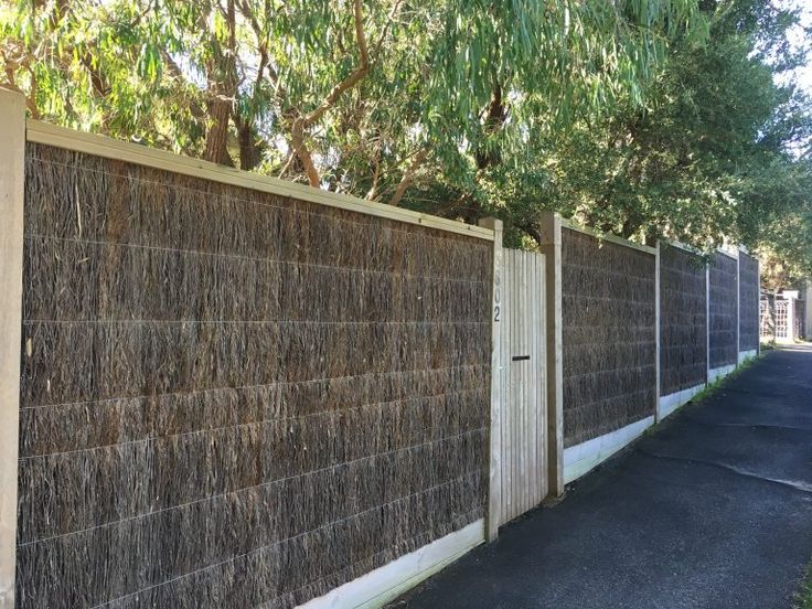 a wooden fence next to a road with trees on both sides and grass covering the wall