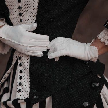 a close up of a person wearing white gloves and black dress with polka dots on it