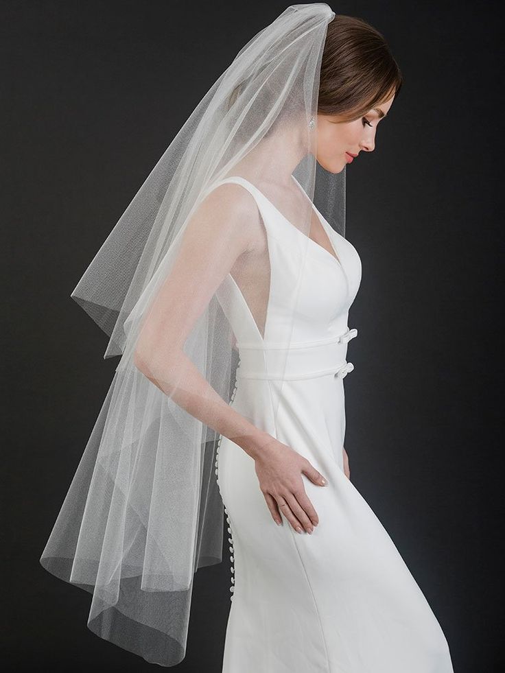 a woman wearing a white wedding dress with a long veil on her head and shoulder