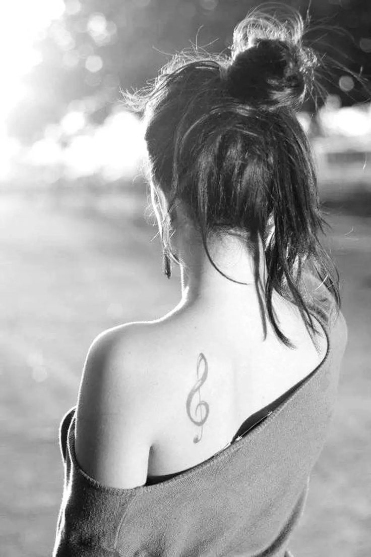 a woman with a musical note tattoo on her upper back shoulder, looking down at the ground