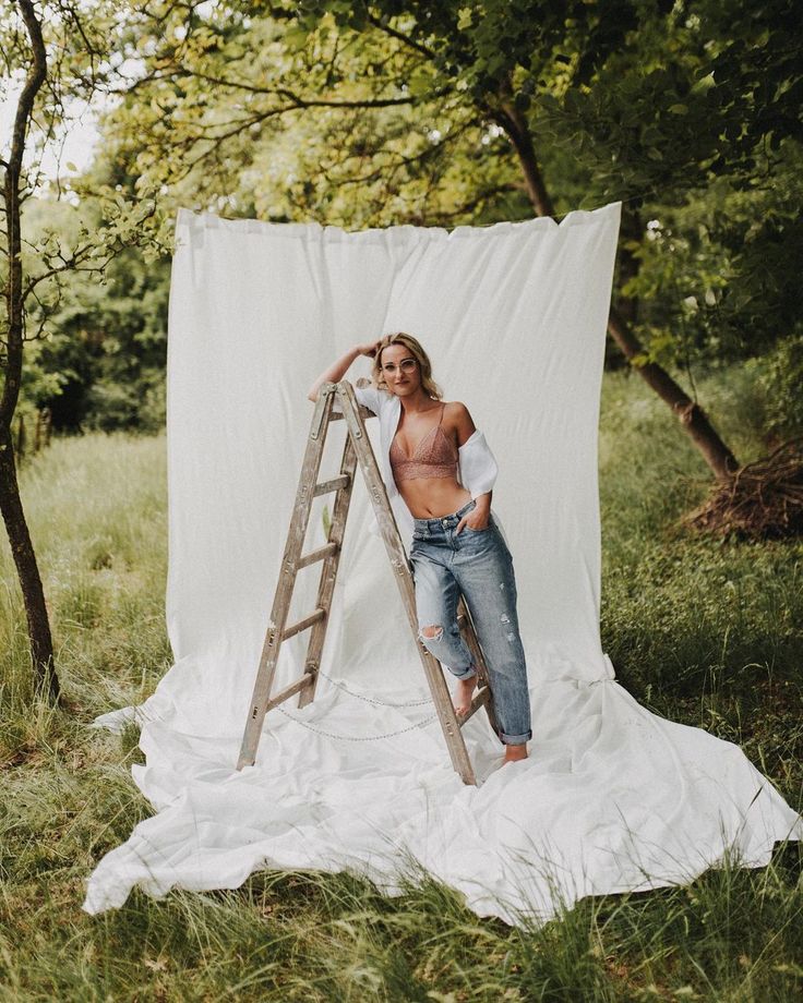 a man standing on top of a ladder next to a white tarp in the woods