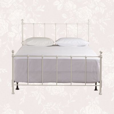 a white metal bed frame with pillows and sheets on it, against a floral wallpapered background