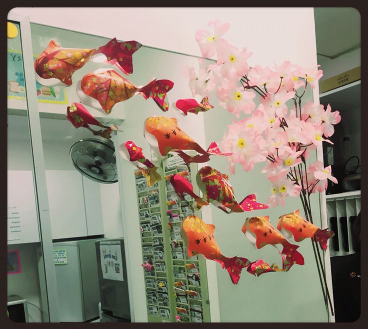 some pink and yellow fish are hanging from a pole in front of a mirror that is decorated with flowers