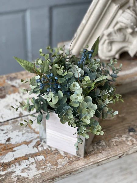 a vase with some plants in it sitting on a wooden table next to a mirror