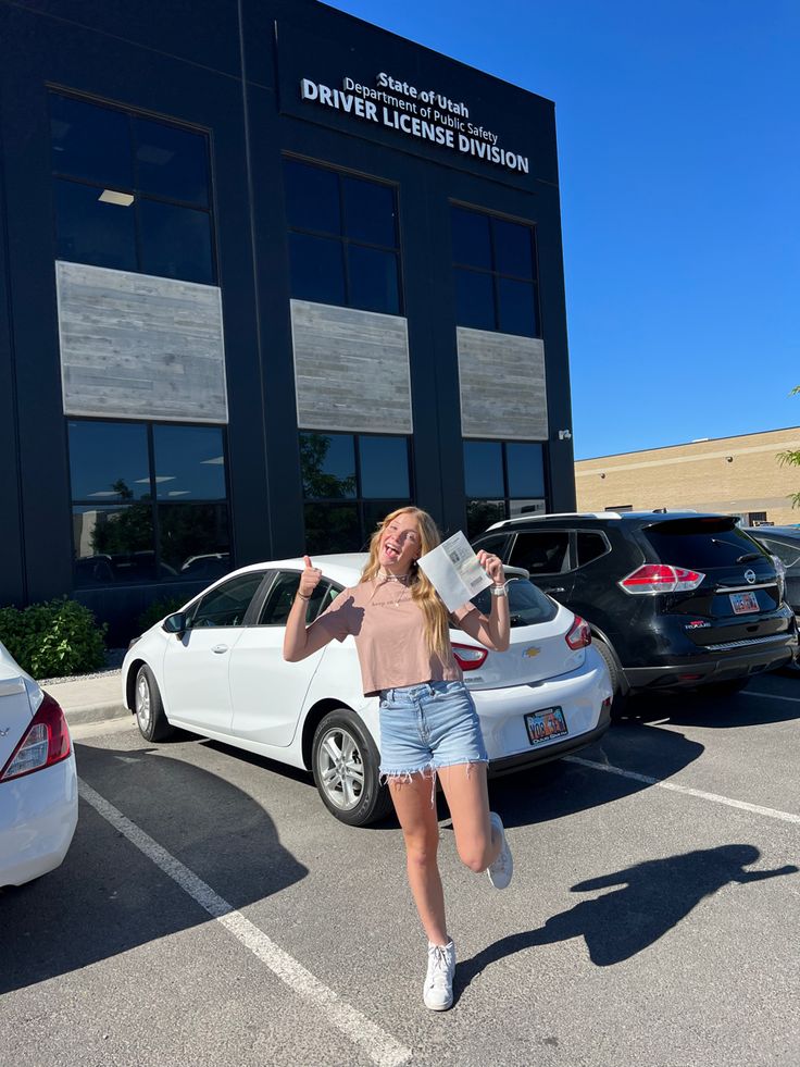 a woman standing in front of a white car with her hand up to the side