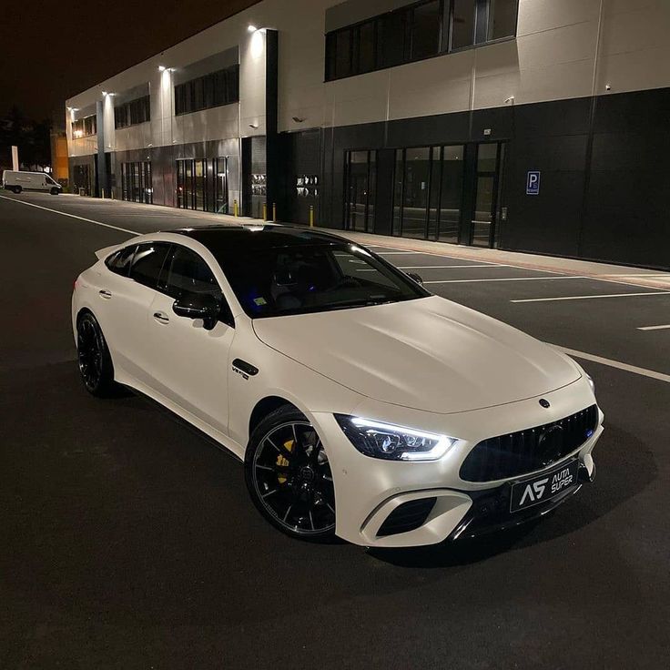 a white sports car parked in front of a building at night with its lights on