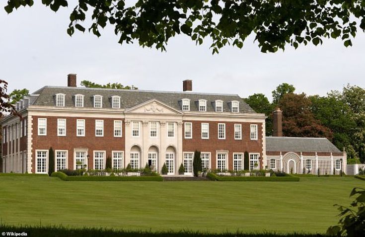 a large red brick building sitting in the middle of a lush green field next to trees