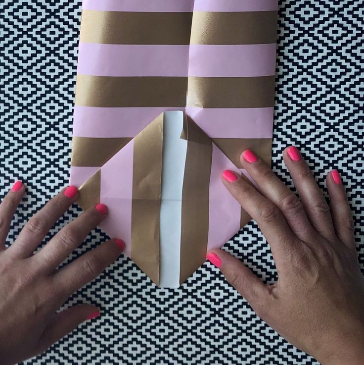 two hands are holding some paper on top of a piece of brown and pink material