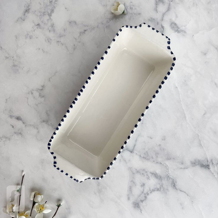 a white dish with blue trim and flowers on the table next to it, sitting on a marble surface