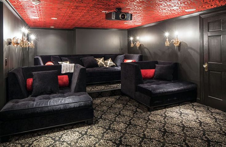 a home theater with black couches and red pillows on the walls, along with chandeliers