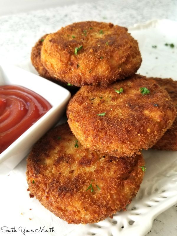 three crab cakes on a plate with ketchup and dipping sauce in the background