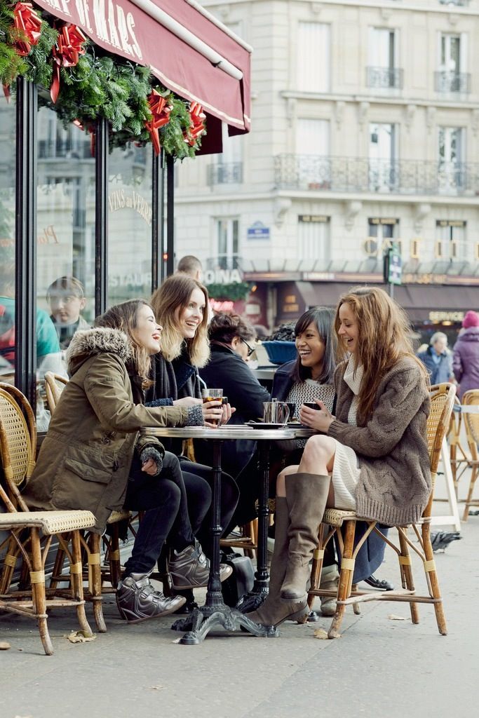 four women sitting at an outdoor cafe talking and drinking coffee in the wintertime,