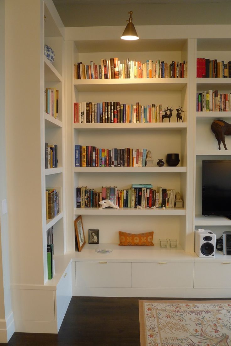 a living room filled with lots of white bookshelves next to a flat screen tv