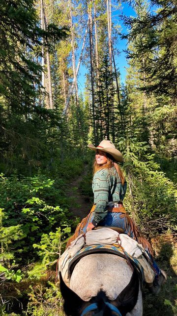 a woman riding on the back of a horse through a forest