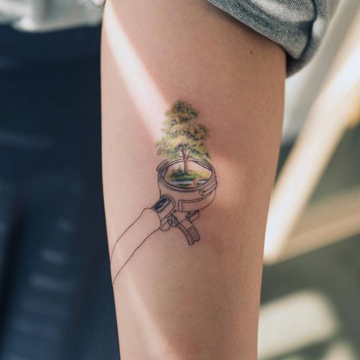 a person with a small tattoo on their arm holding a potted plant in it's hand