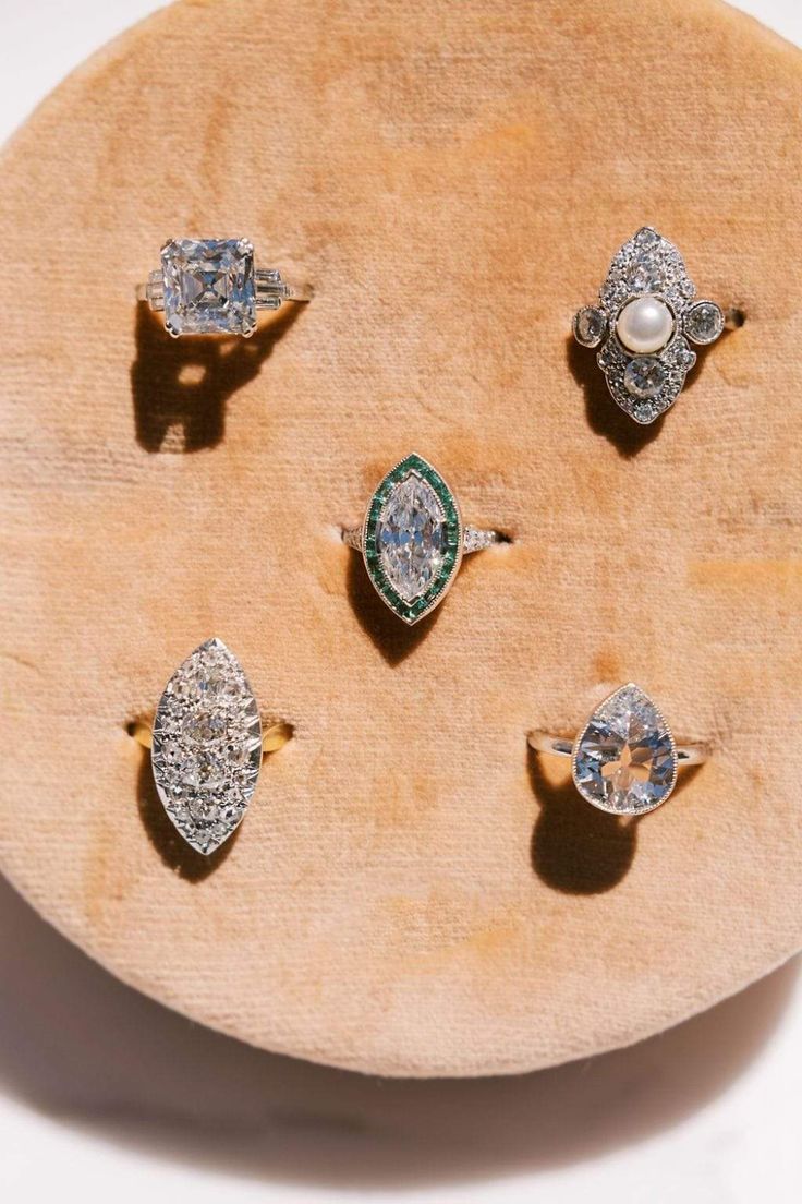 five different rings sitting on top of a wooden display plate with white and green stones