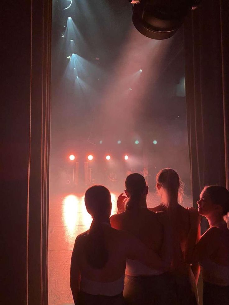 four people standing in front of a stage with lights on it and their arms around each other