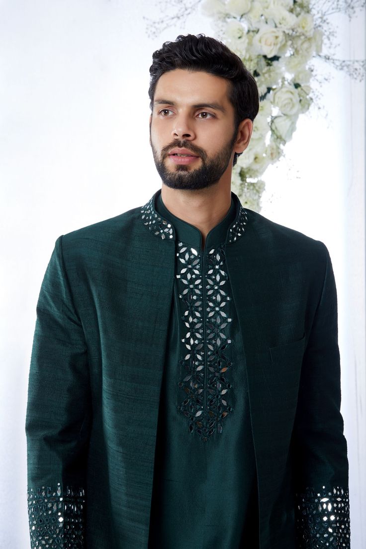 This emerald green open sherwani set features mirror work detailing on the neck and on the cuffs of the sherwani. It compliments the detailing of mirror work yoke of a silk kurta paired with a brocade trouser. Complimenting footwear is also available. From Seema Gujral's Tuscan Summer collection. DELIVERY TIMEPlease allow 8-12 weeks for your outfit to arrive.FABRIC DETAILSRaw SilkProfessional cleaning only. Emerald Green Sherwani, Mirror Work Neck Designs For Kurti, Mirror Work Kurta For Men, Brocade Trousers, Open Sherwani, Marriage Dresses, Tuscan Summer, India Fashion Men, Jodhpuri Suits