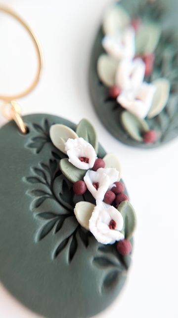 two earrings with flowers on them sitting on top of a white table next to each other