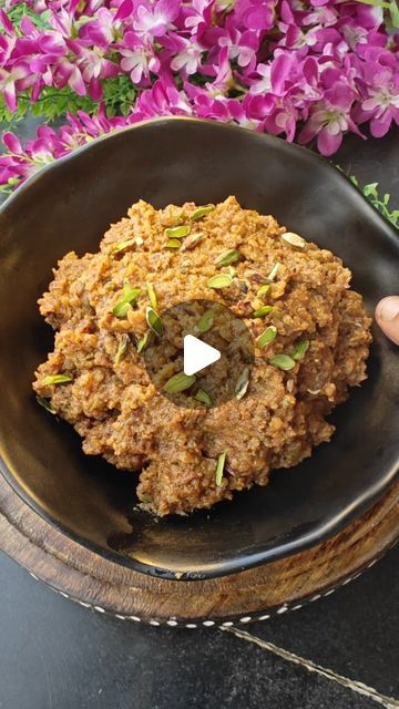 a black bowl filled with food on top of a wooden table next to purple flowers