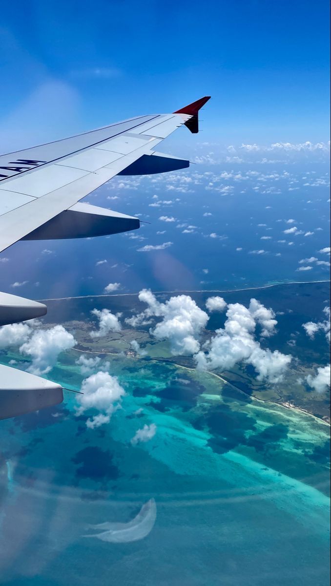 an airplane wing flying over the ocean and clouds